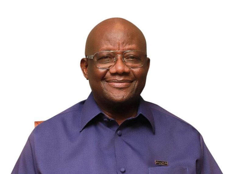 Smiling man with glasses in a purple button-down shirt, against a white background (head-and-shoulders portrait).