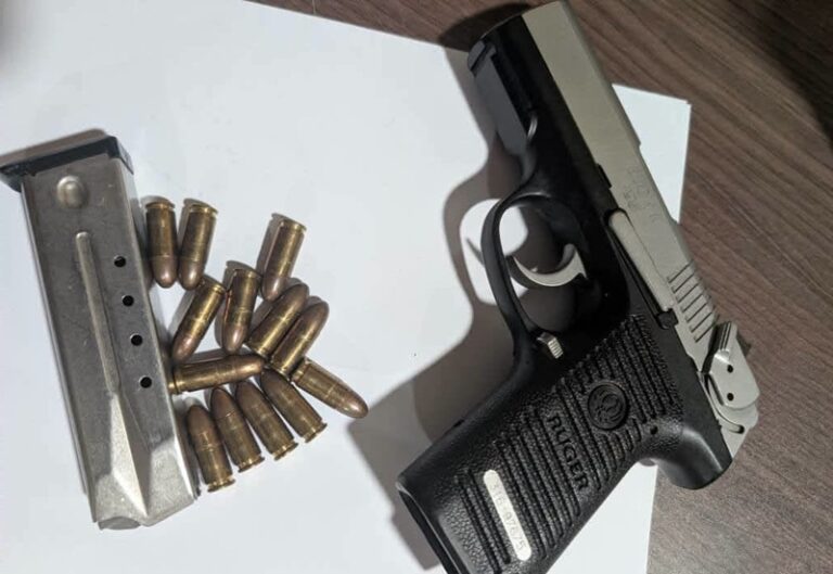 Black semi-automatic handgun with a magazine and loose cartridges on a white surface.