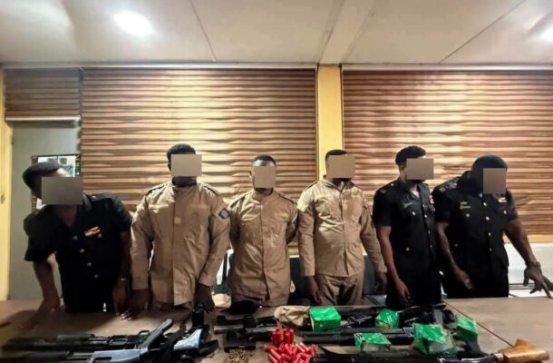 Six uniformed officers stand behind a table displaying rifles, ammunition, and green boxes of ammo.