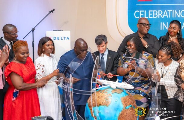 A diverse group of officials and staff cutting a globe sculpture with a small airplane model at a ceremonial event, Delta branding visible.
