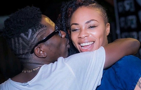 Two friends share a warm hug; a man with glasses in a white shirt embraces a smiling woman in blue.