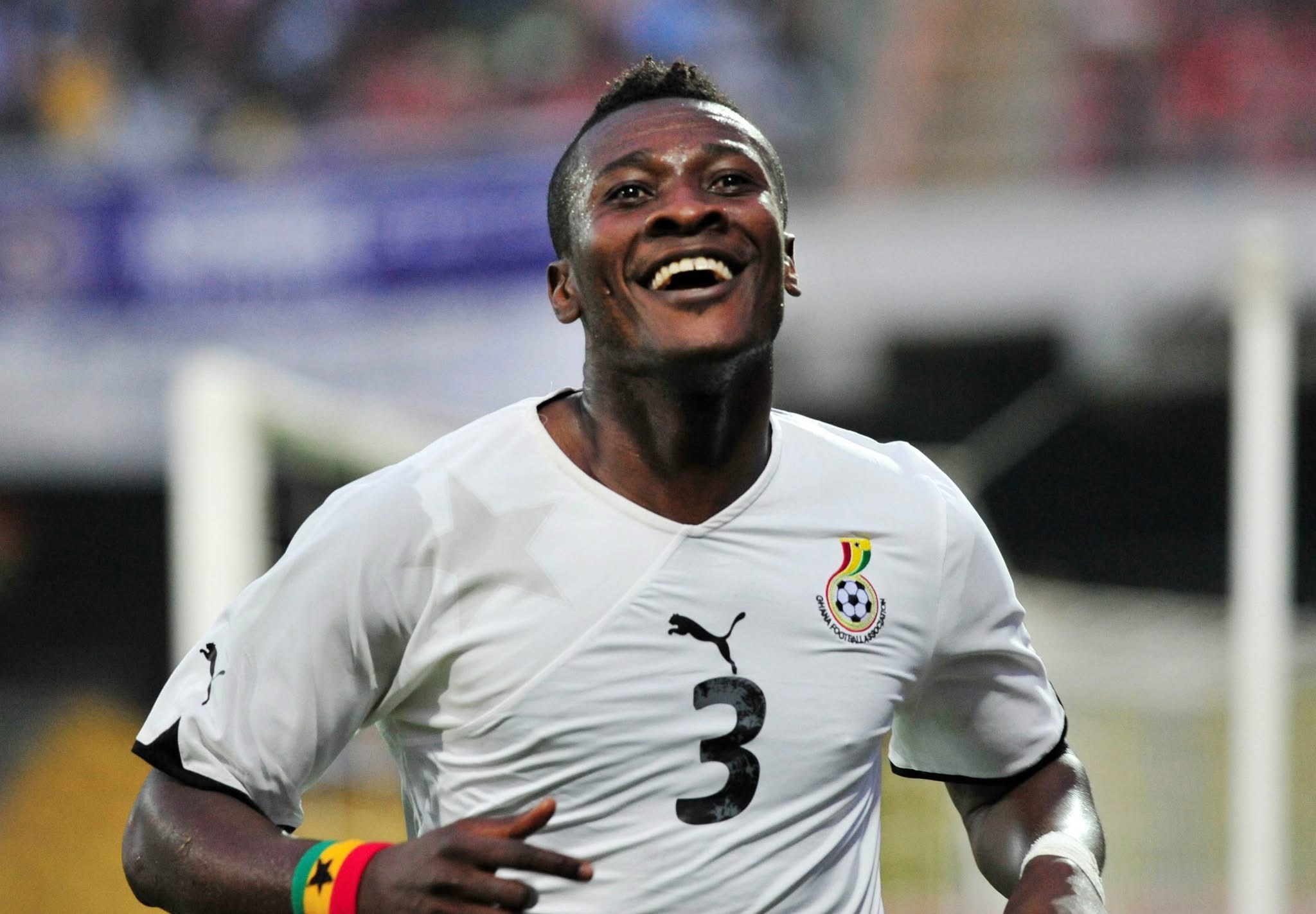 Jubilant footballer in a white jersey with Senegal crest, running and smiling on the pitch after a goal.