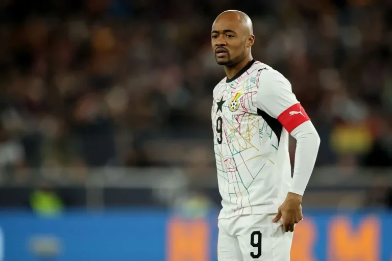 Male soccer player standing on the field in a white jersey with colorful geometric lines and the number 9, wearing a red captain's armband.
