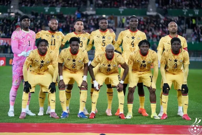 Ghana national football team posing for a group photo on the field in yellow kits with a black star badge.