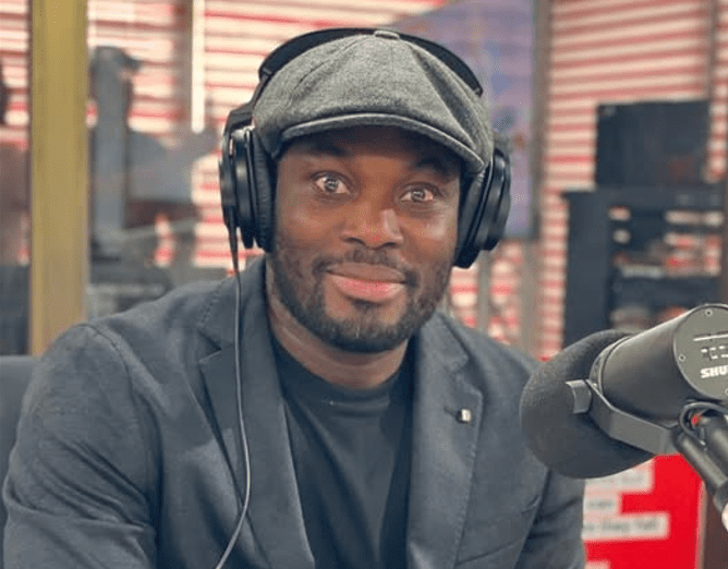 Man wearing a flat cap and large headphones, speaking into a microphone in a radio studio.