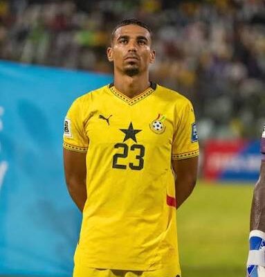 Soccer player in a yellow jersey with the number 23, standing with hands behind his back on the field during a match.