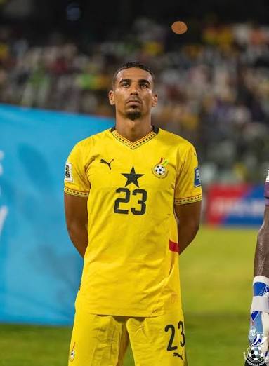 Soccer player in a yellow jersey with the number 23, standing with hands behind his back on the field during a match.