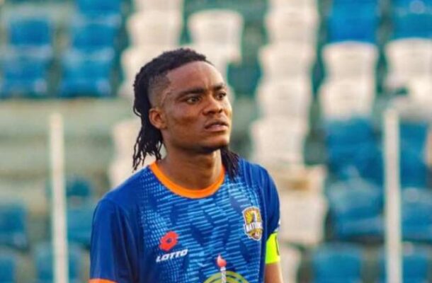 Soccer player in a blue jersey with orange trim and a captain's armband on the field.