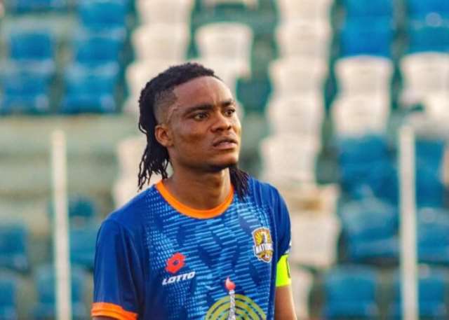 Soccer player in a blue jersey with orange trim and a captain's armband on the field.