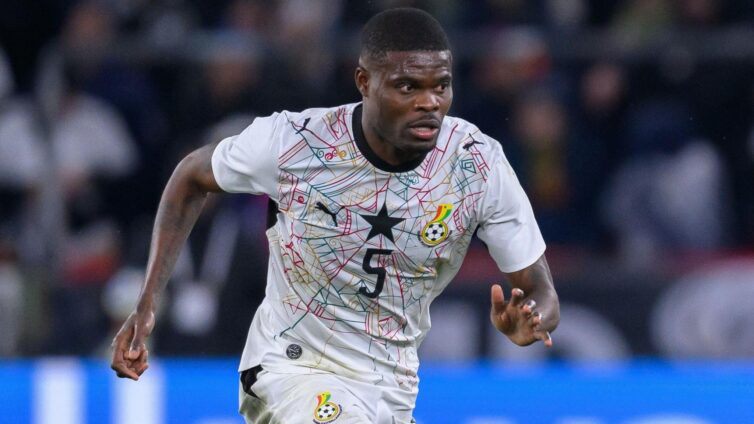 Ghana national team footballer sprinting on the field in a white geometric jersey with a black star crest.