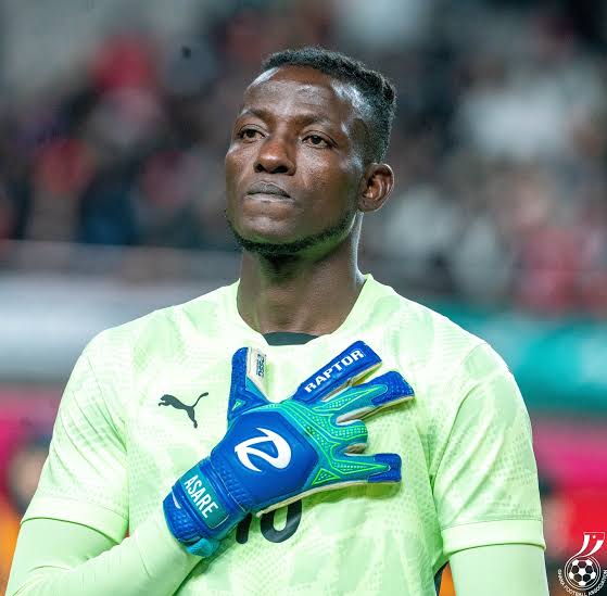 Soccer goalkeeper in neon green jersey poses with blue gloves, hand over heart, on the field during a match.