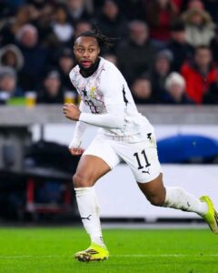 Soccer player in white kit with number 11 sprinting on the green field during a match.