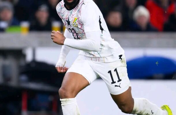 Ghana national team footballer in a white kit with the number 11, sprinting on a green pitch with neon yellow boots.
