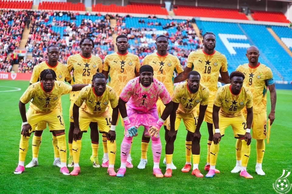 Soccer team in yellow kits posing for a group photo on the field, with a pink goalkeeper standing center front.