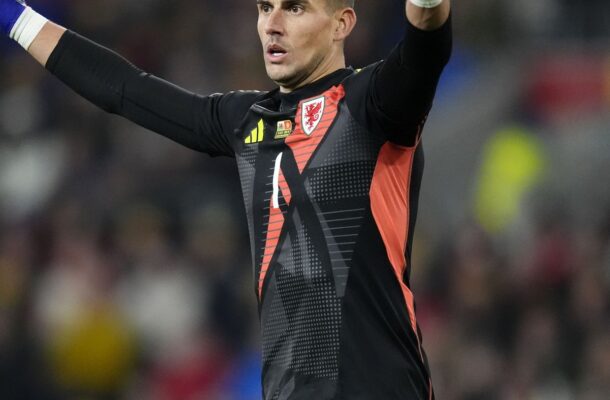 Welsh national team goalkeeper in black-red kit with gloves, arms raised in celebration on the pitch.
