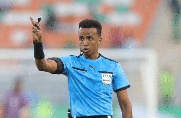 IMG_0866 | Ghanaguardian.com Referee in a blue kit raises a whistle and points during a soccer match, signaling a call.
