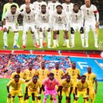 Soccer players in white uniforms form a lineup on the field before a match, with one team standing behind the other in yellow kits for a group photo.