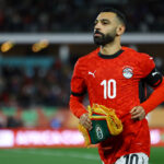 Soccer player in a red jersey with number 10 holding a ceremonial trophy on the field.