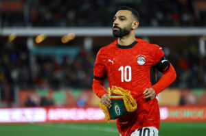 Soccer player in a red jersey with number 10 holding a ceremonial trophy on the field.