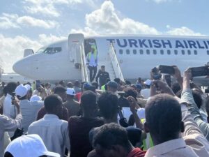 Crowd of people with phones raised greeting passengers as a Turkish Airlines plane arrives and people exit via portable stairs.
