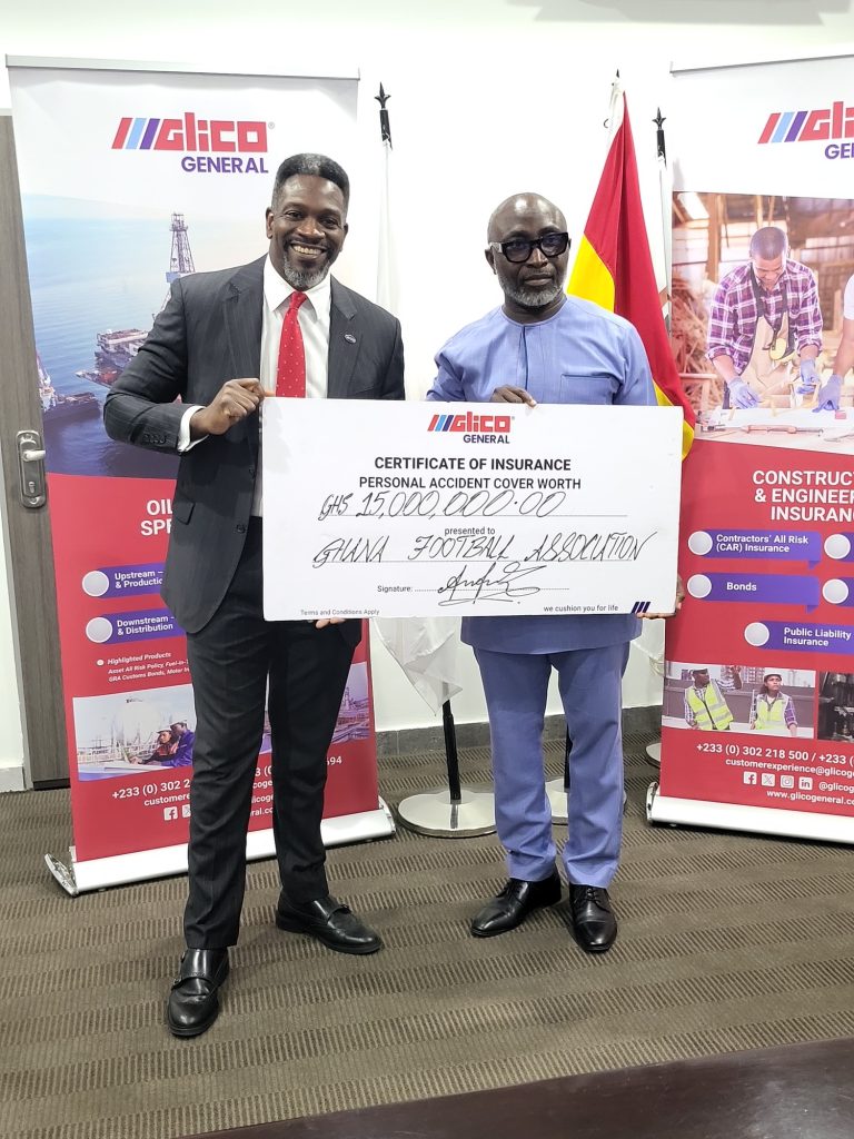 Two men in formal and traditional attire hold a large ceremonial cheque for GH₵15,000,000 in front of Glico General banners with a Ghana flag nearby.