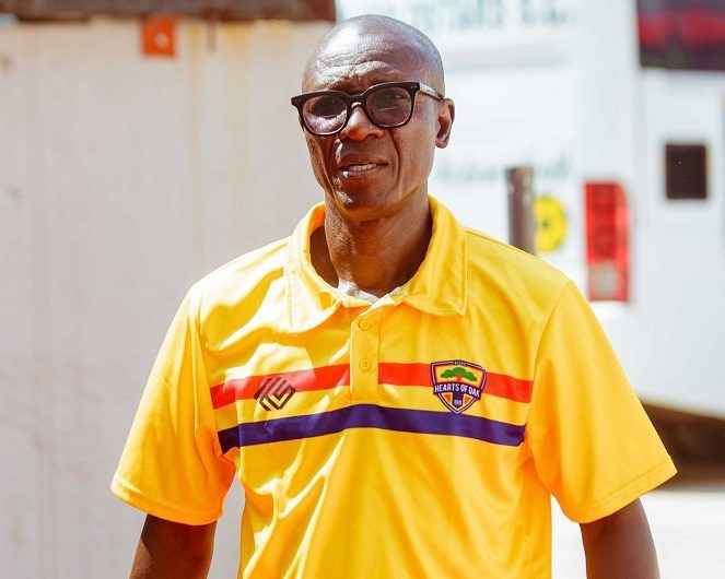 Smiling man in a bright yellow polo with red and blue stripes, wearing glasses outdoors.