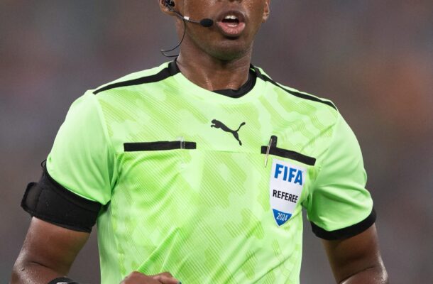 Male soccer referee running, wearing a bright green FIFA jersey with a headset mic and armband.