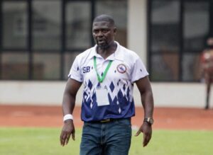Athletic man wearing a white and blue polo with a medal around his neck on a sports field