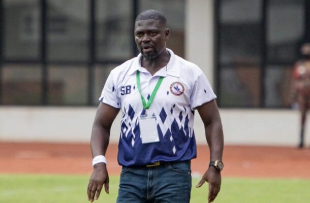 Athletic man wearing a white and blue polo with a medal around his neck on a sports field