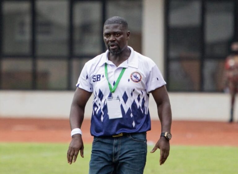 Athletic man wearing a white and blue polo with a medal around his neck on a sports field