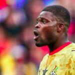 Soccer player in a yellow jersey shouting on the field with a blurred stadium crowd in the background.