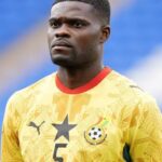 Male footballer in a yellow Ghana national team jersey with a black star emblem and number 5, standing on the field with a serious expression.