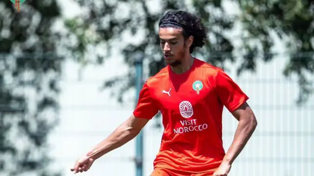 Soccer player in a red jersey dribbling on a sunny training field with a Visit Morocco logo on the chest