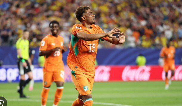 Soccer player in an orange jersey with number 15 celebrates on the field, arms outstretched.