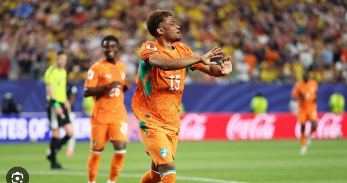 Soccer player in an orange jersey with number 15 celebrates on the field, arms outstretched.