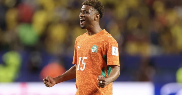 Soccer player in an orange jersey with number 15 celebrating with clenched fists on the field.