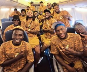 Group of athletes in matching orange camouflage shirts posing for a photo inside an airplane.