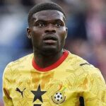 Portrait of a footballer in a yellow jersey with a black star badge, on a soccer field, looking upward to the left.