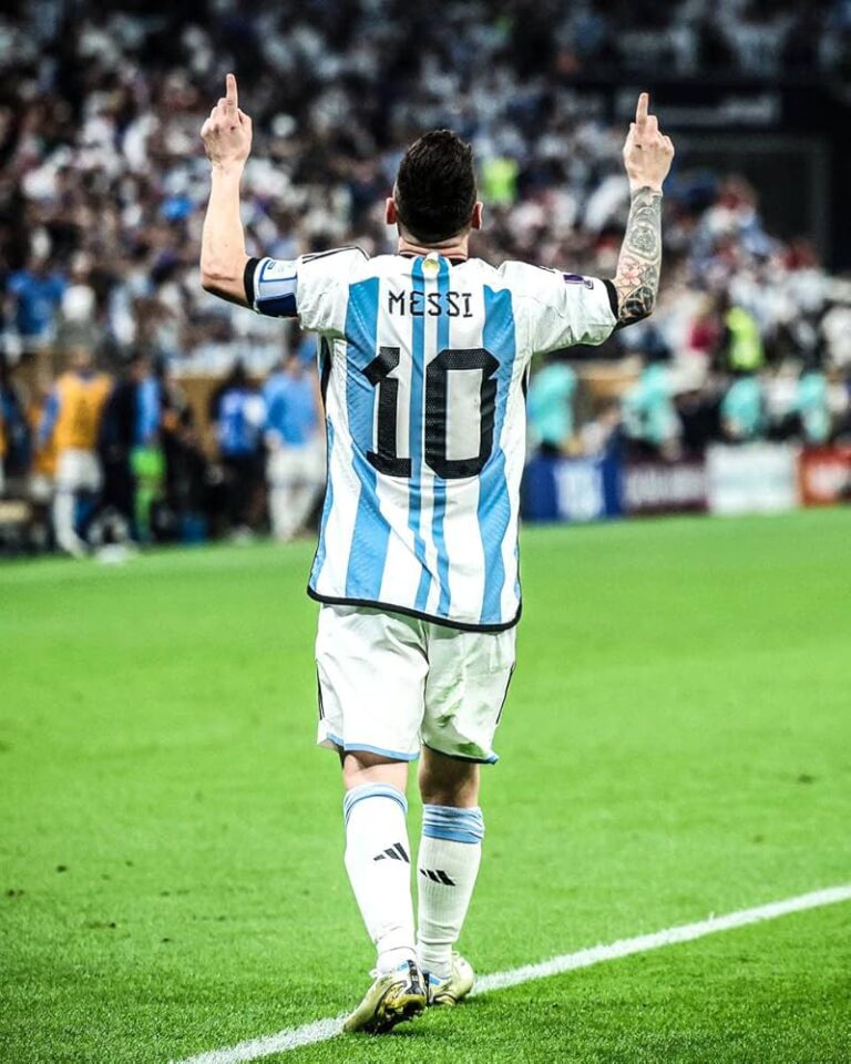 Argentina footballer Messi (No. 10) raises both arms in celebration on the field, back view with fans in the stands.