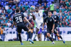 Soccer player in a white jersey with number 8 leaps to control the ball while two dark-clad defenders approach.