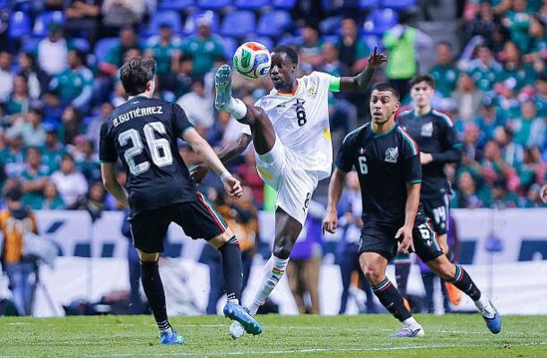Soccer player in a white jersey with number 8 leaps to control the ball while two dark-clad defenders approach.