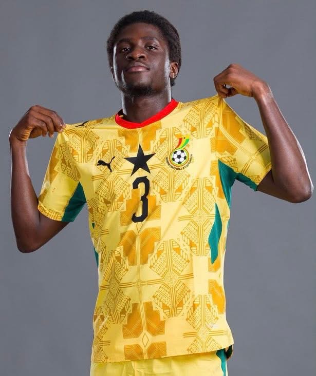 Young male soccer player posing in a yellow jersey with number 3, pulling the sides to show the shirt, against a gray backdrop.