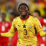 Ghana national team defender wearing yellow jersey with star and number 3, arms outstretched in celebration on a rainy stadium field