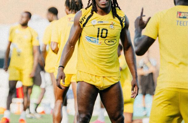 Soccer players in yellow uniforms on a green field; a smiling player with braids watches a colorful ball overhead.