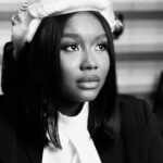 Black-and-white portrait of a woman in a blazer and white blouse, wearing a knit beret and looking upward to the right.