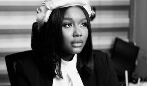 Black-and-white portrait of a woman in a blazer and white blouse, wearing a knit beret and looking upward to the right.