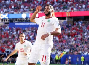Soccer player wearing a white jersey number 11 salutes the crowd during a World Cup match, with a packed stadium behind him.
