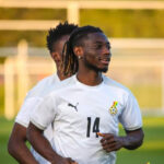 Soccer player in a white jersey with number 14, running on a practice field with goals in the background.