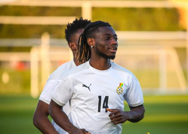 Soccer player in a white jersey with number 14, running on a practice field with goals in the background.