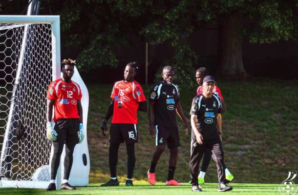 IMG_1018 | Ghanaguardian.com Soccer players stand by the goalpost on a sunny green field, wearing red and black uniforms, ready for a match or practice.